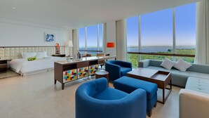 Ein modernes Hotelzimmer mit einem großen Bett, einem Schreibtisch, einer Sitzecke und Meerblick.