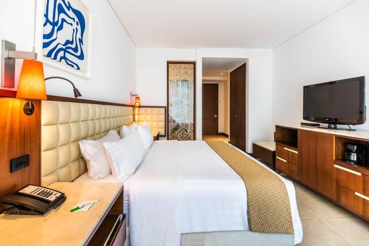 A hotel room with a large bed, bedside lamps, a television, a desk with a telephone, and a decorative wall piece.