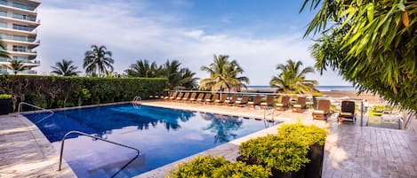 A swimming pool with lounge chairs, surrounded by greenery and a view of the ocean.
