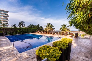 A swimming pool with lounge chairs, surrounded by greenery and a view of the ocean.
