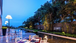An outdoor dining area with tables and chairs, a pool, and surrounding greenery.