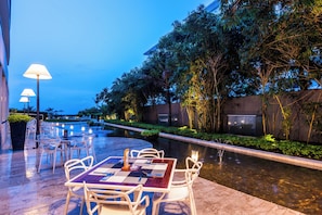 An outdoor dining area with tables and chairs, a pool, and surrounding greenery.