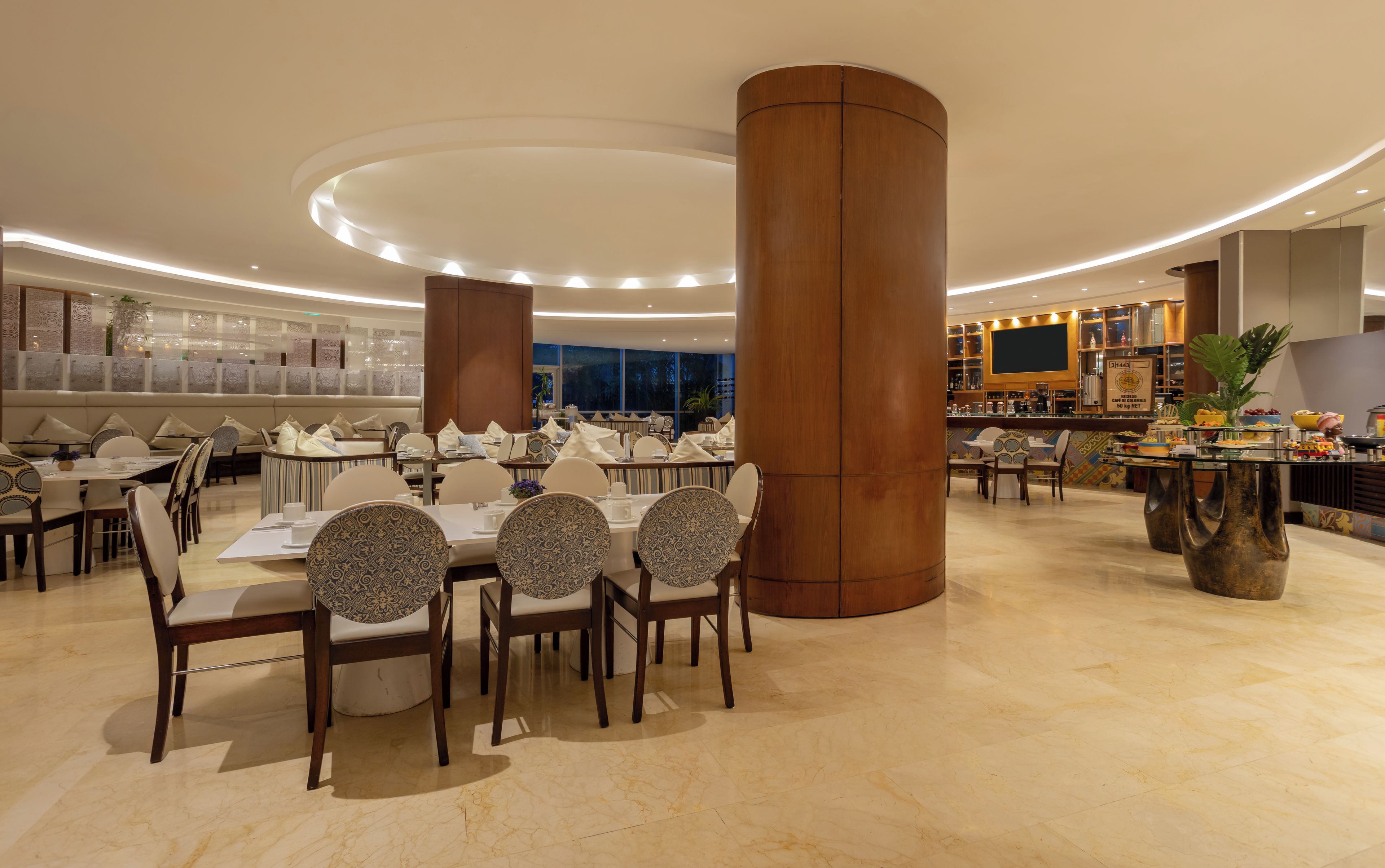 Un comedor amplio con mesas y sillas redondas, altos pilares de madera y una zona de bar moderna.