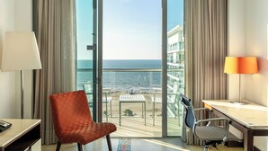 Ein Hotelzimmer mit Balkon, Schreibtisch, zwei Stühlen und Meerblick.