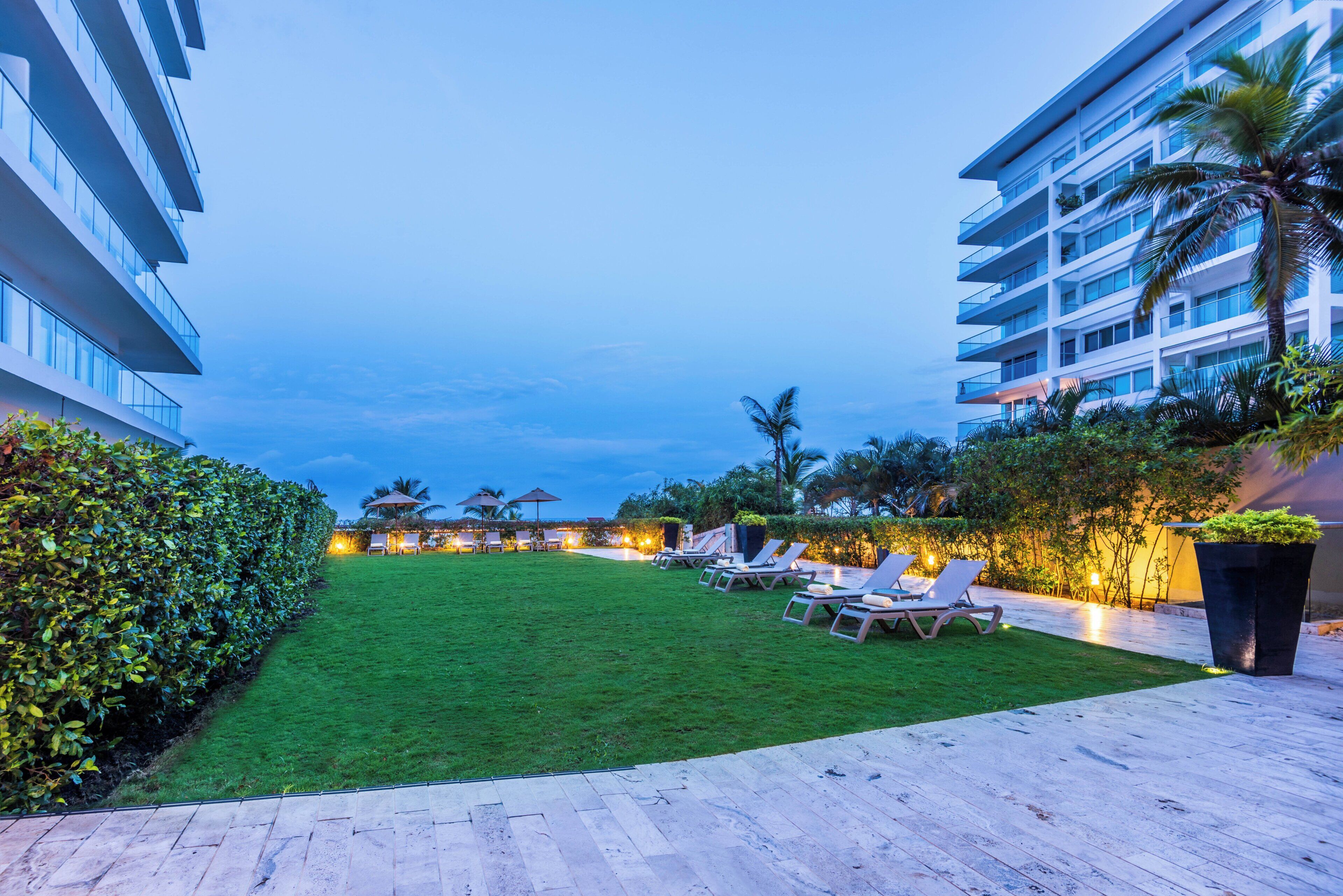 A hotel courtyard with a well-maintained lawn, lounge chairs, and a pool area.