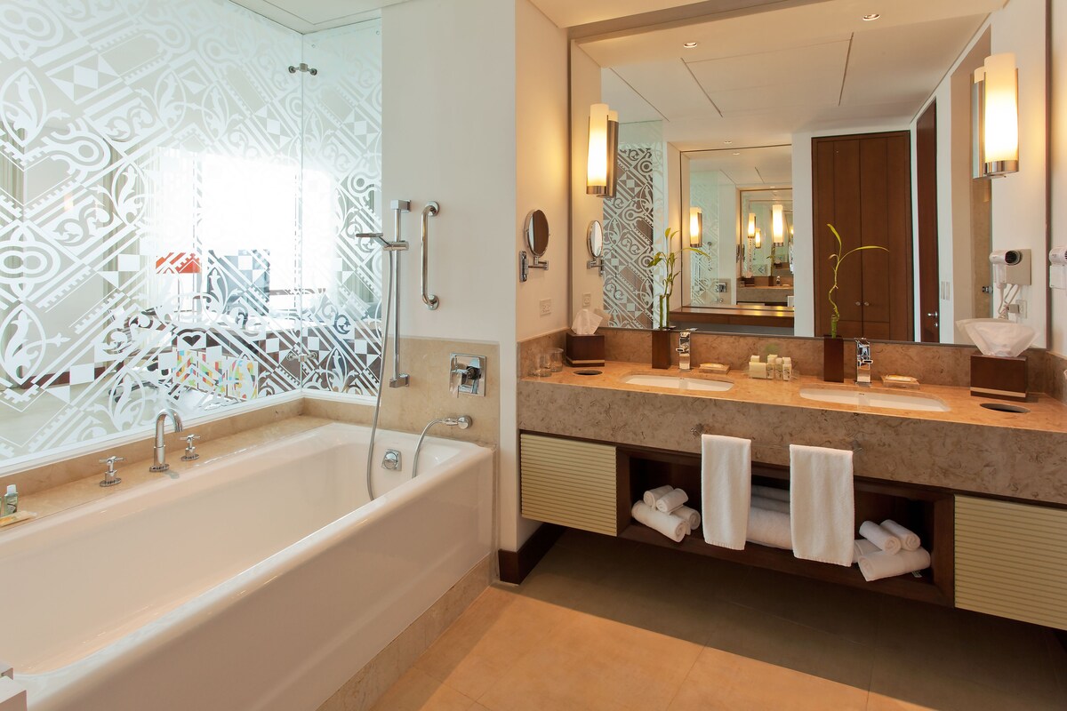 A modern bathroom with a large bathtub, dual sinks, and a vanity with towels.