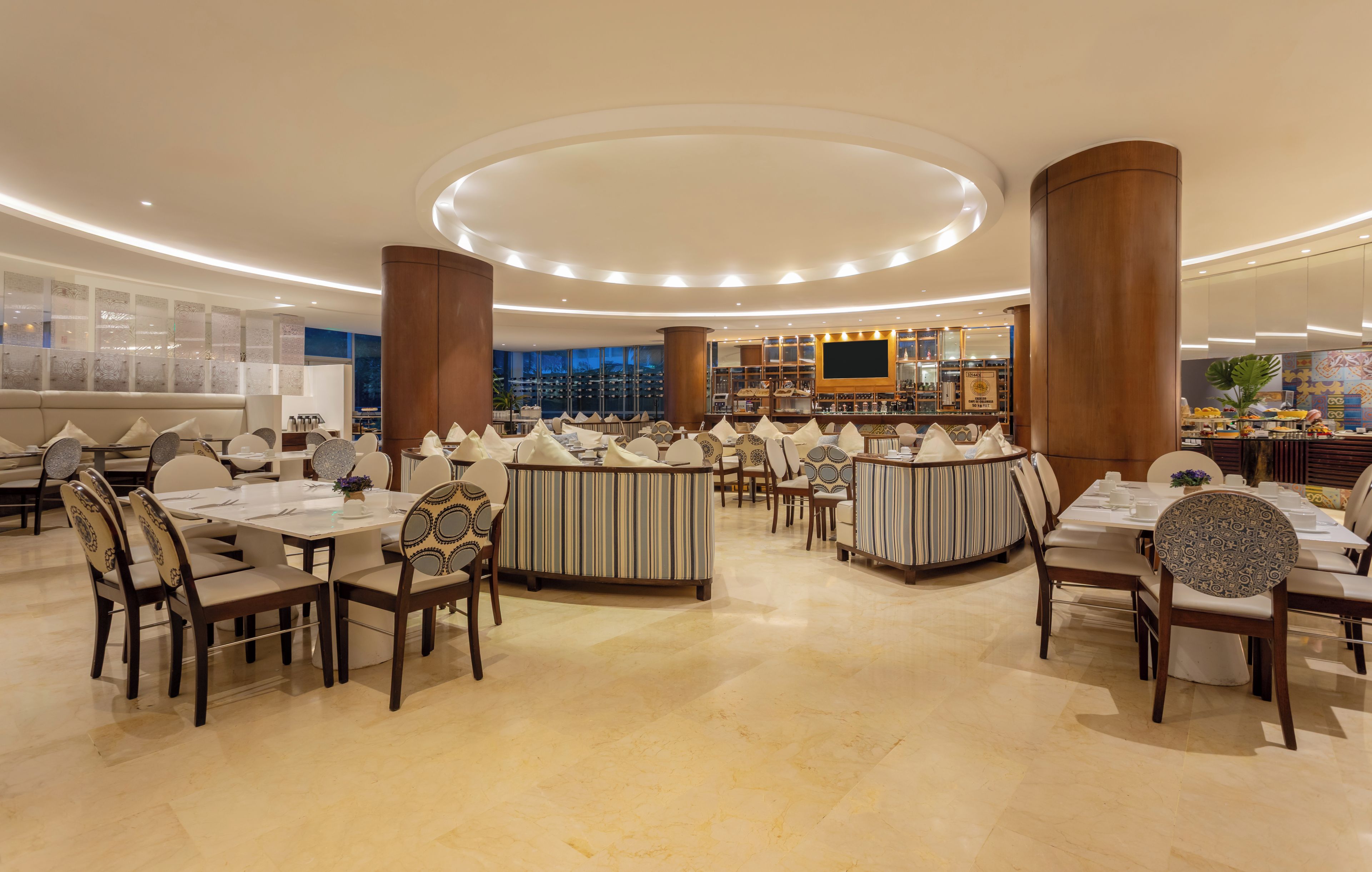 A spacious restaurant with round tables and booths, a bar area, and a view of the cityscape.