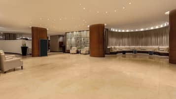 Un'ampia hall con un'area salotto a forma di curva, una reception e una pianta di grandi dimensioni.