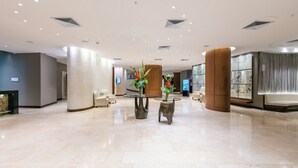 Eine großzügige Lobby mit einem polierten Marmorboden, einem zentral platzierten Glastisch mit Vasen und einem modernen Deckenbau.