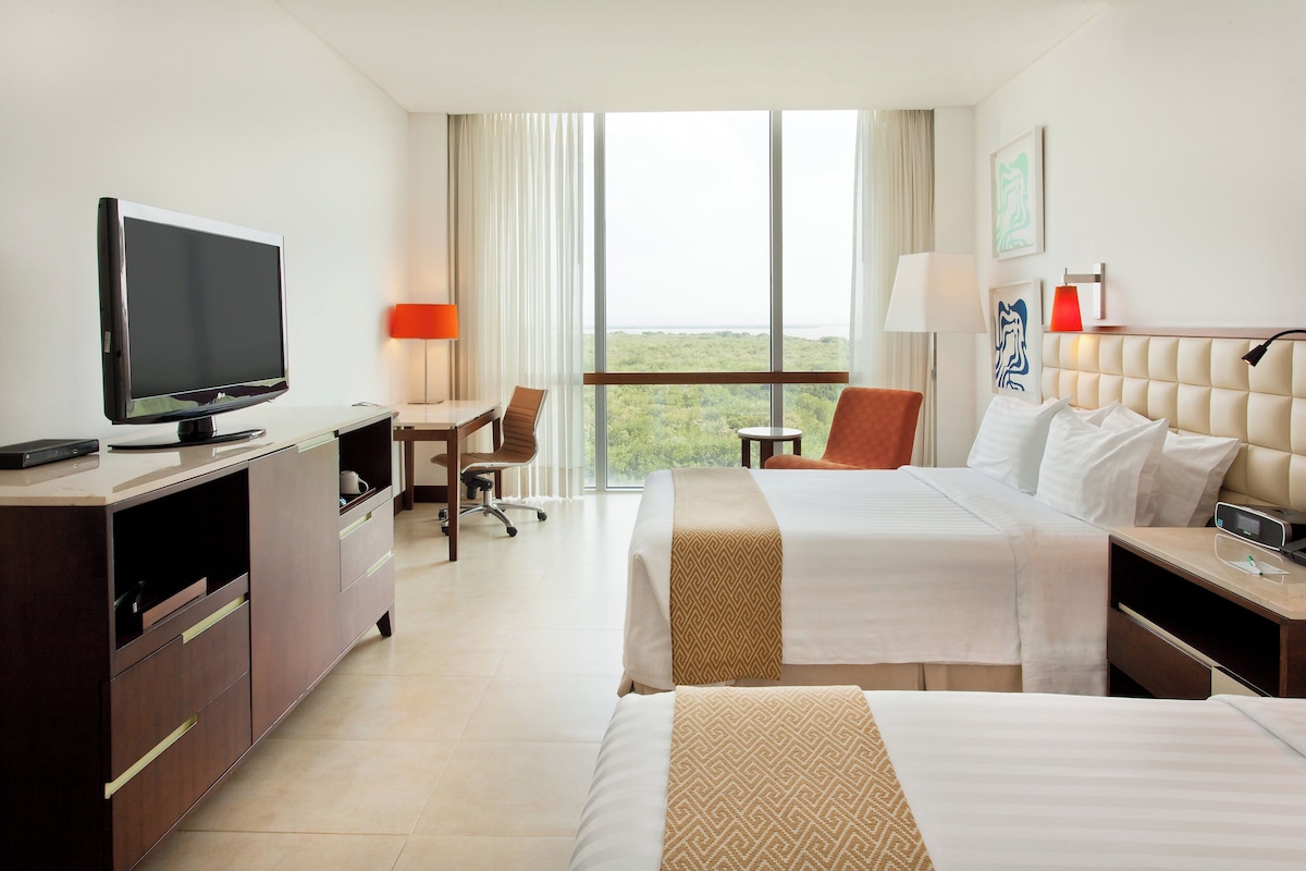 A hotel room with a television, two beds, a desk, and a view of the outdoors.
