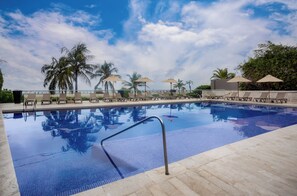 A swimming pool with lounge chairs and umbrellas, surrounded by palm trees.