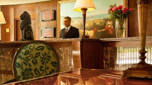 A reception desk with a lion statue, framed certificates, a painting, and a vase with flowers.