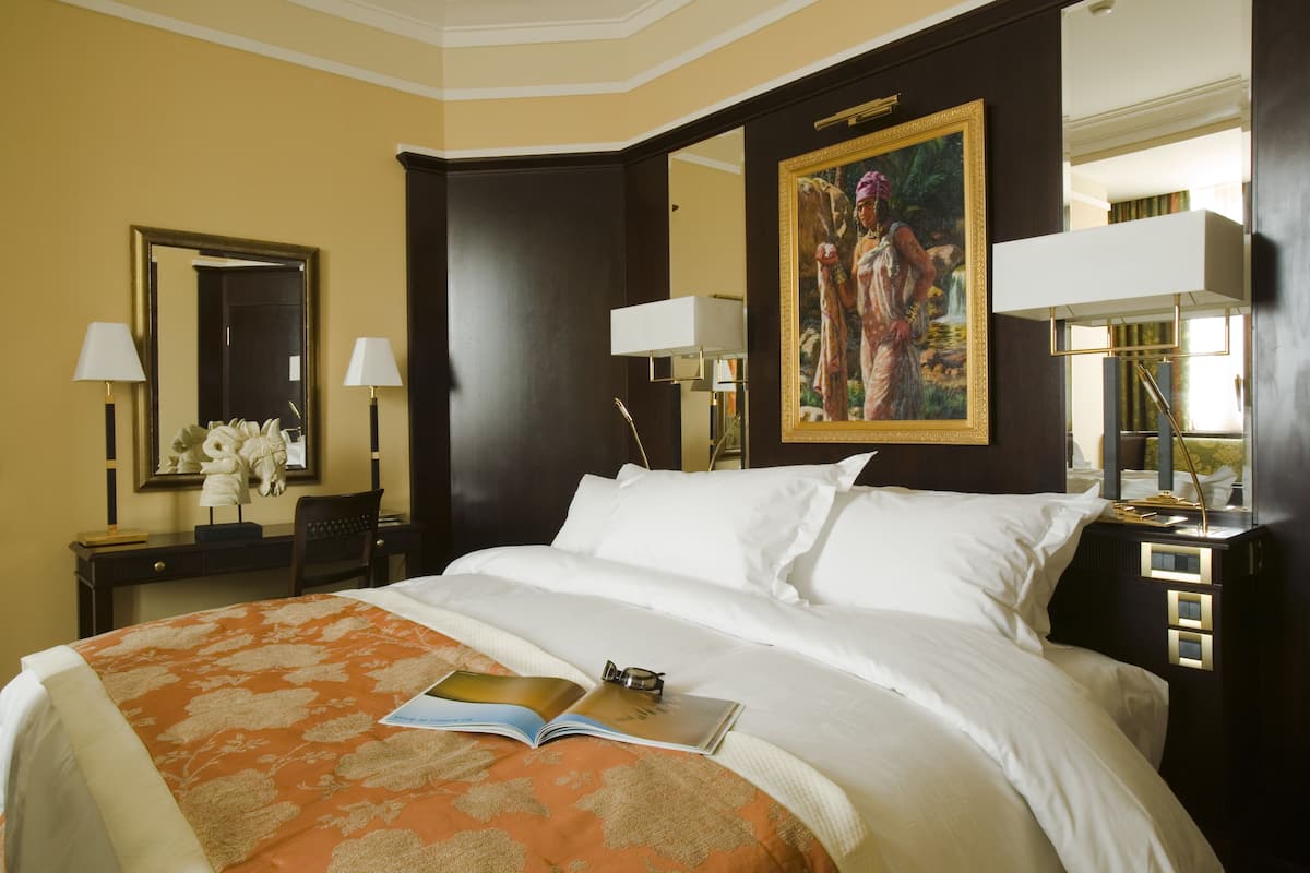 Une chambre d’hôtel avec un grand lit, deux lampes de chevet, une table de chevet avec une lampe, un tableau au mur et un bureau avec une chaise.