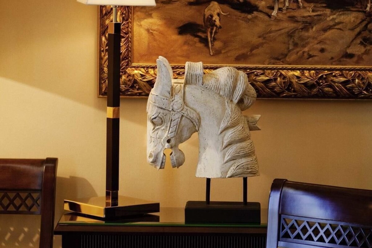 A sculpture of a horse's head on a stand, a lamp, and a framed painting on the wall.