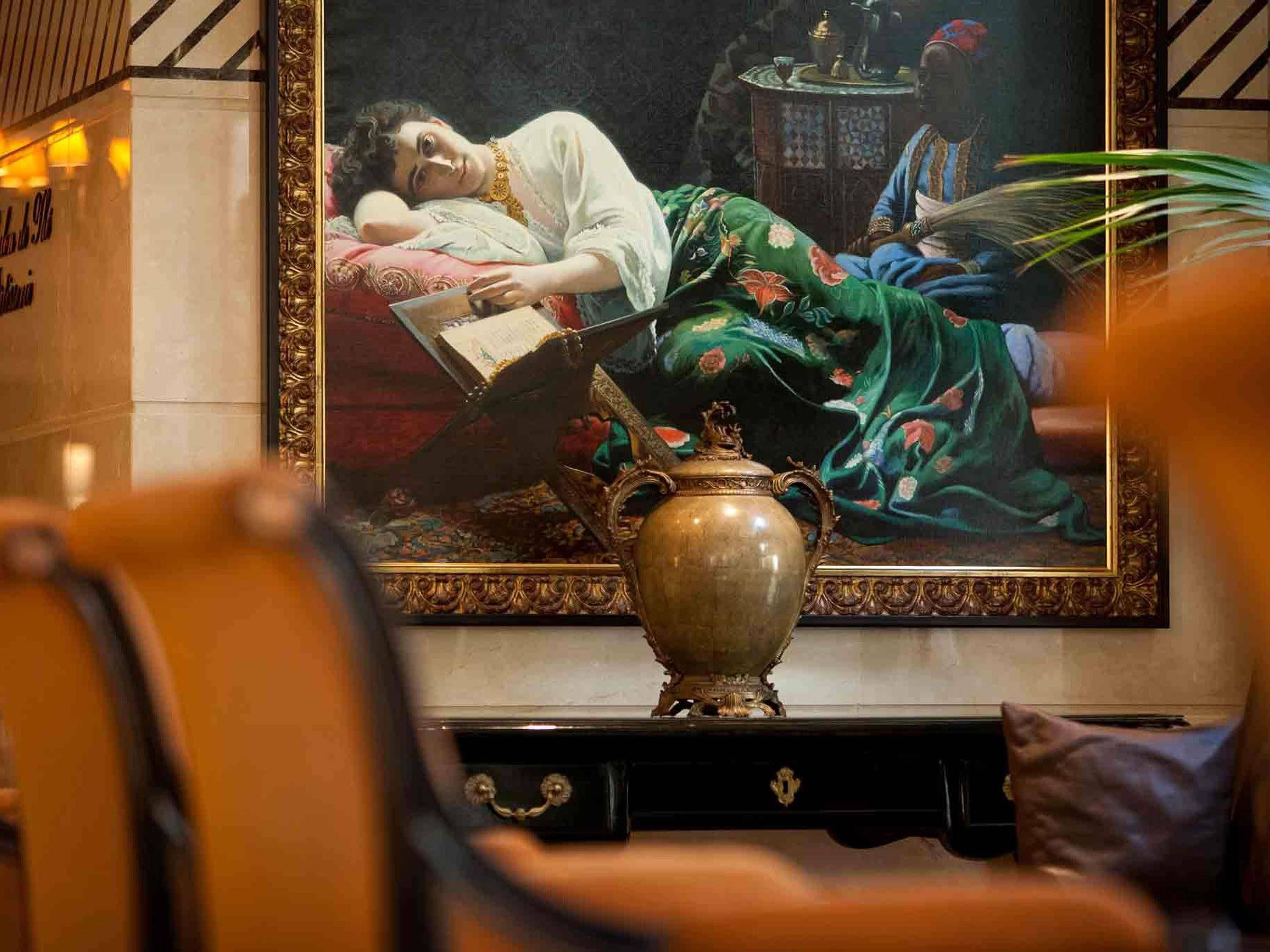 A room with a large painting of a woman reading, a decorative vase, and a patterned rug.