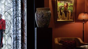 A room with a decorative metal gate, a large vase on a pedestal, a framed painting, a lamp, and a leather armchair.