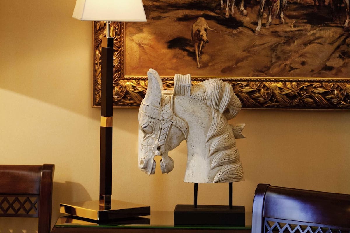 Une sculpture posée sur un piédestal, une lampe et un tableau accroché au mur.