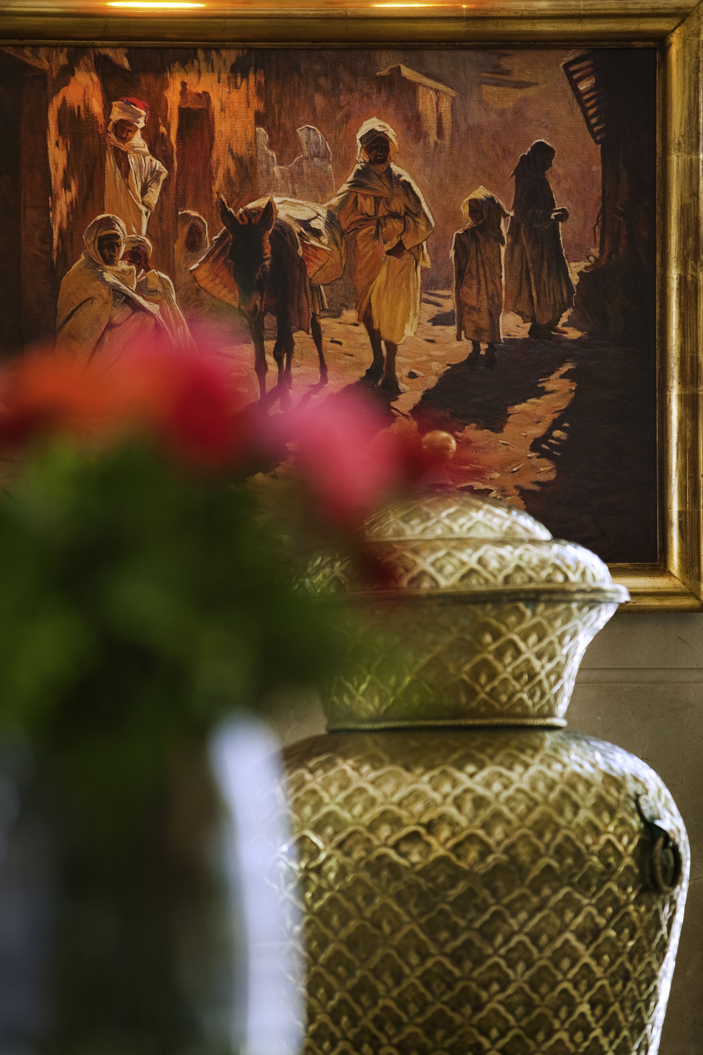 A framed painting of a historical scene with figures and a donkey, a decorative vase, and a blurred foreground.