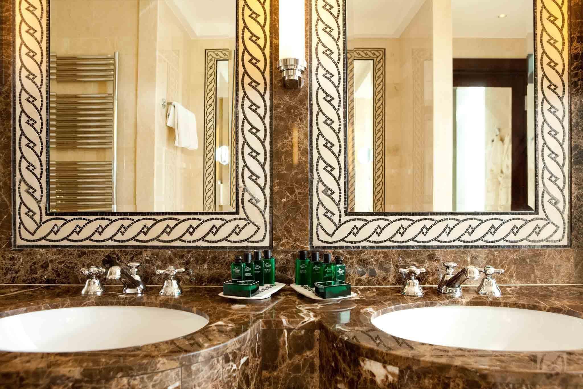 A bathroom with two sinks, a towel rack, and a mirror with decorative borders.