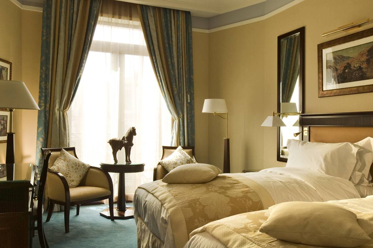 Une chambre d’hôtel avec un grand lit, une chaise, une petite table sur laquelle est posée une figurine de cheval, et une lampe.