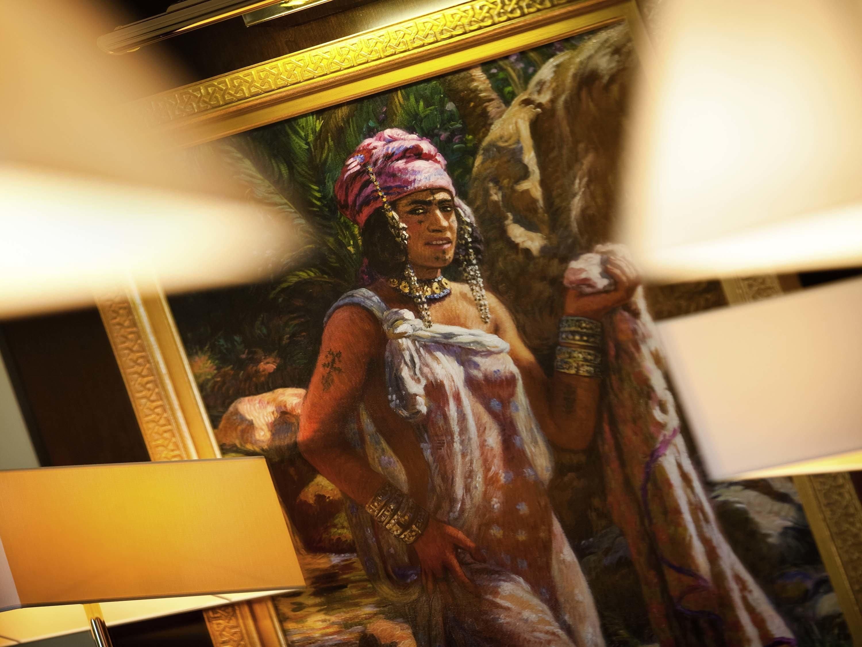 A framed painting of a person in traditional attire, a lamp, and a patterned carpet.