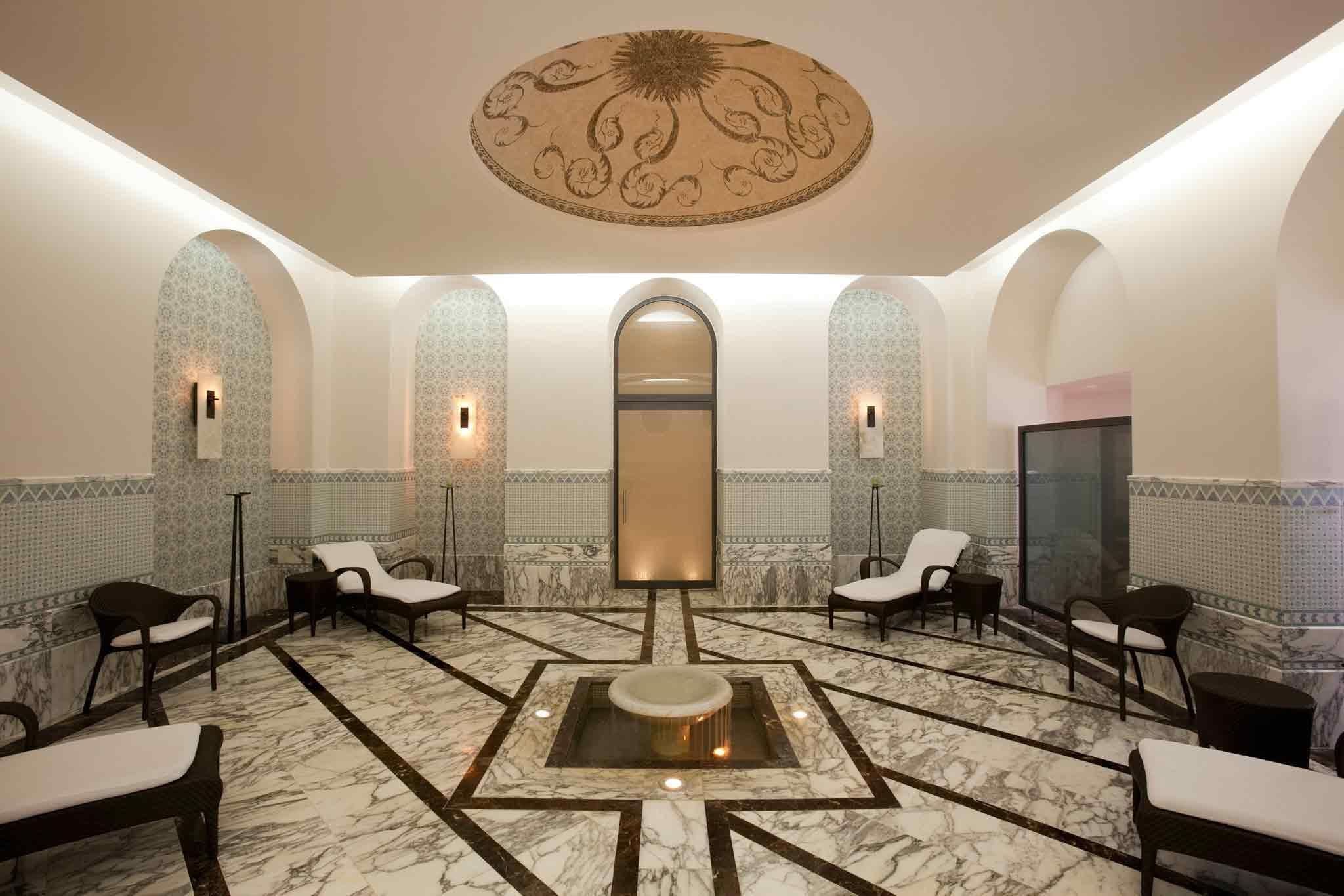 A spa room with a central hot tub, seating areas, and a decorative ceiling.