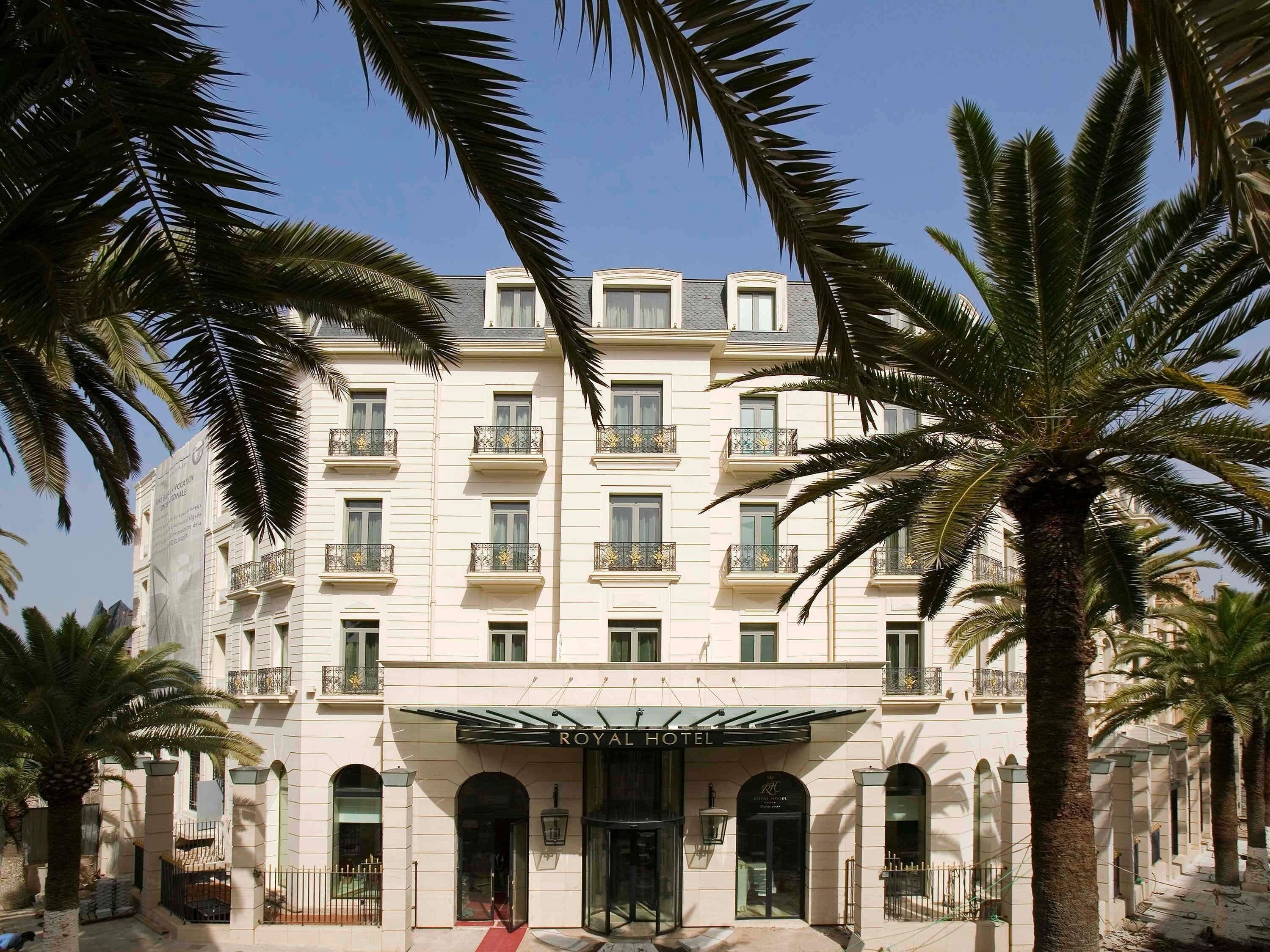 Hotel de diversos pisos amb balcons, entrada central i palmeres.