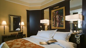 A hotel room with a large bed, two bedside lamps, a nightstand, a mirror, and a painting on the wall.