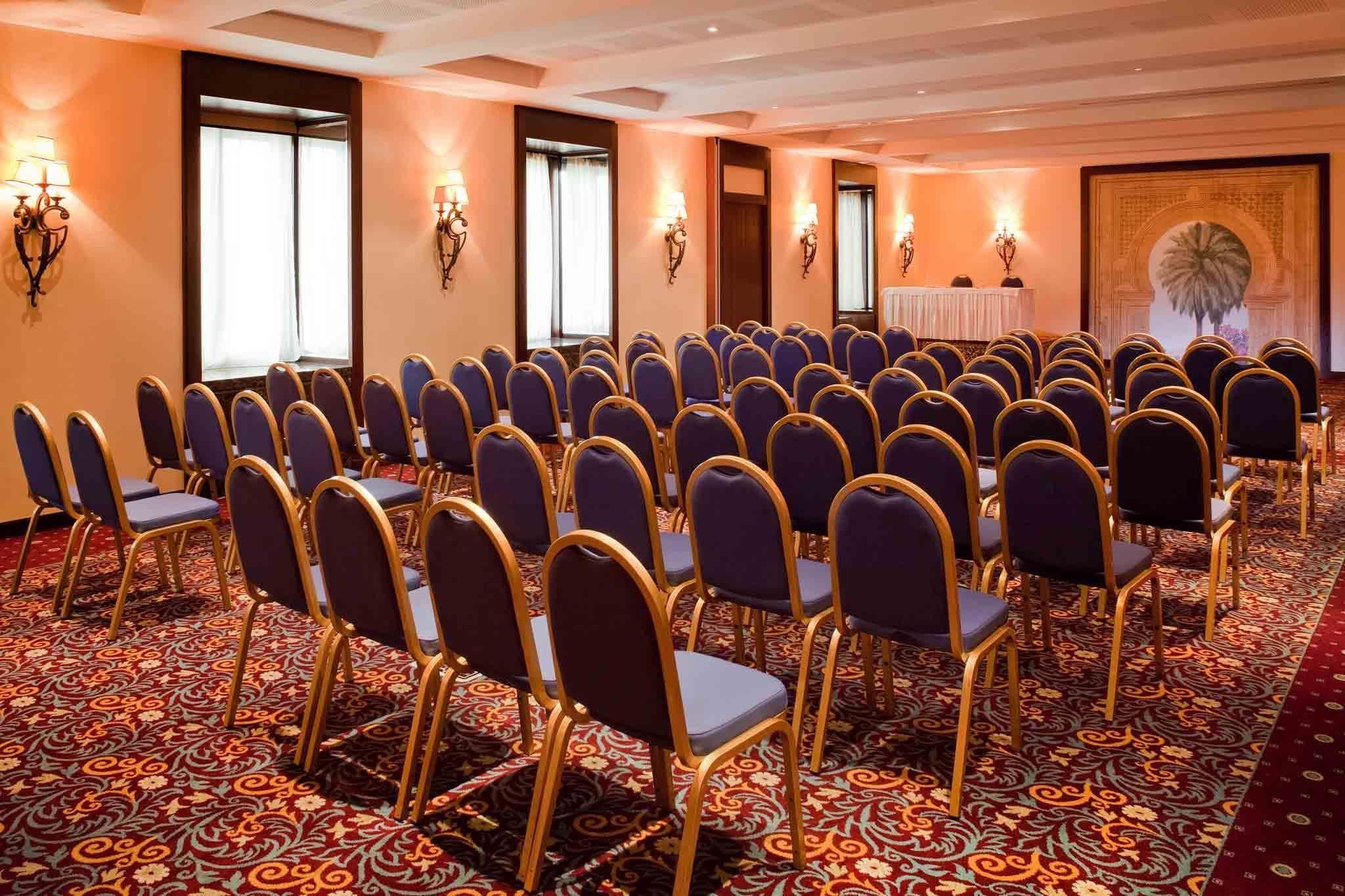 A conference room with rows of chairs, a podium, and wall sconces.
