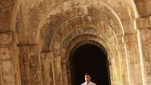 Un homme marchant dans un couloir bordé d’arches en pierre.