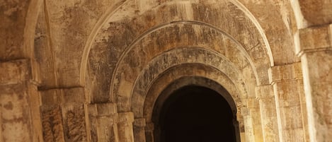 A man walking through a corridor with stone arches.