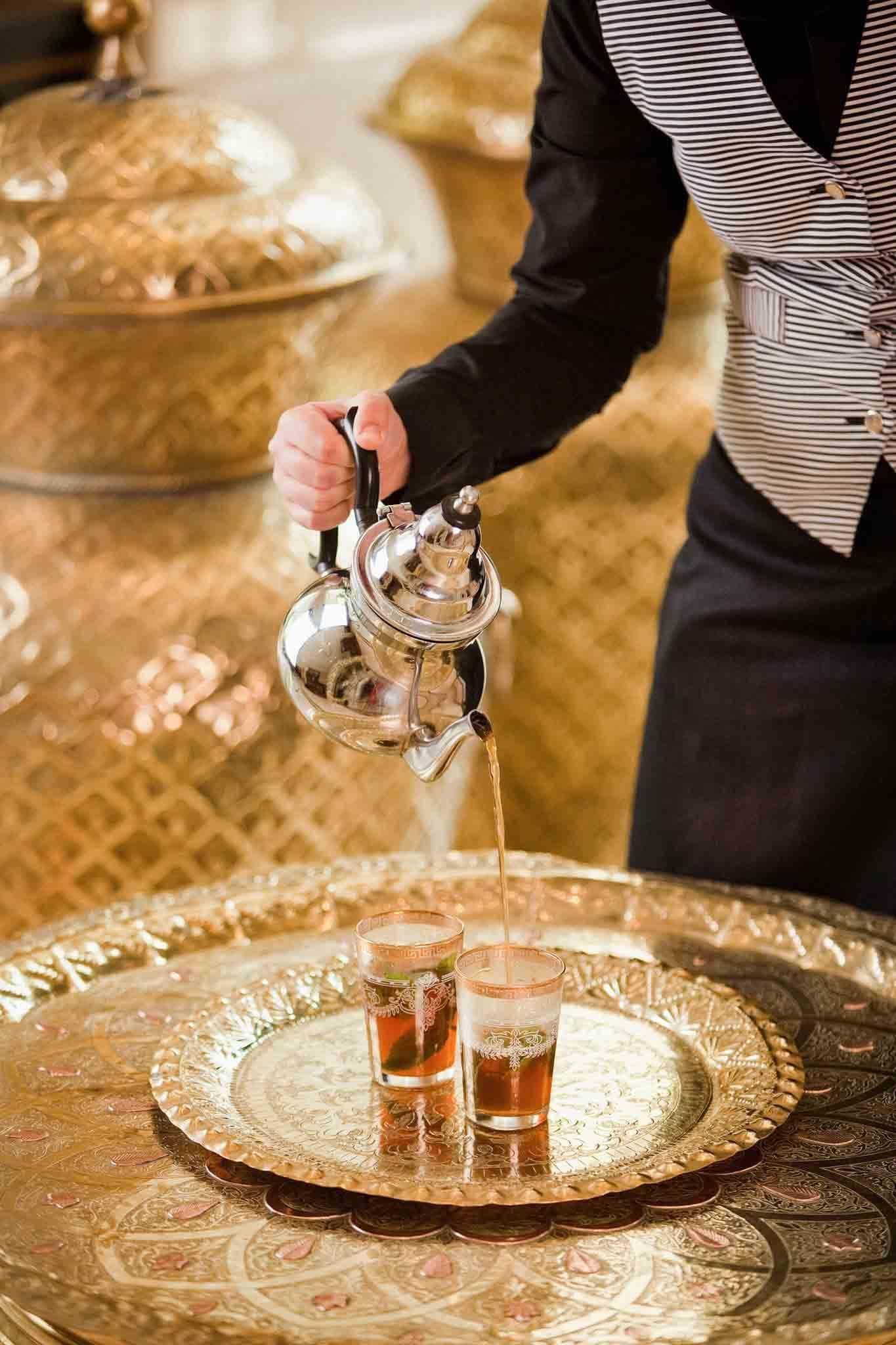 Una persona sirve té en vasos sobre una bandeja decorativa.