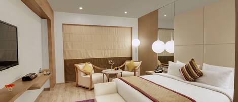 A modern hotel room with a large bed, a sofa, a desk, and a TV.