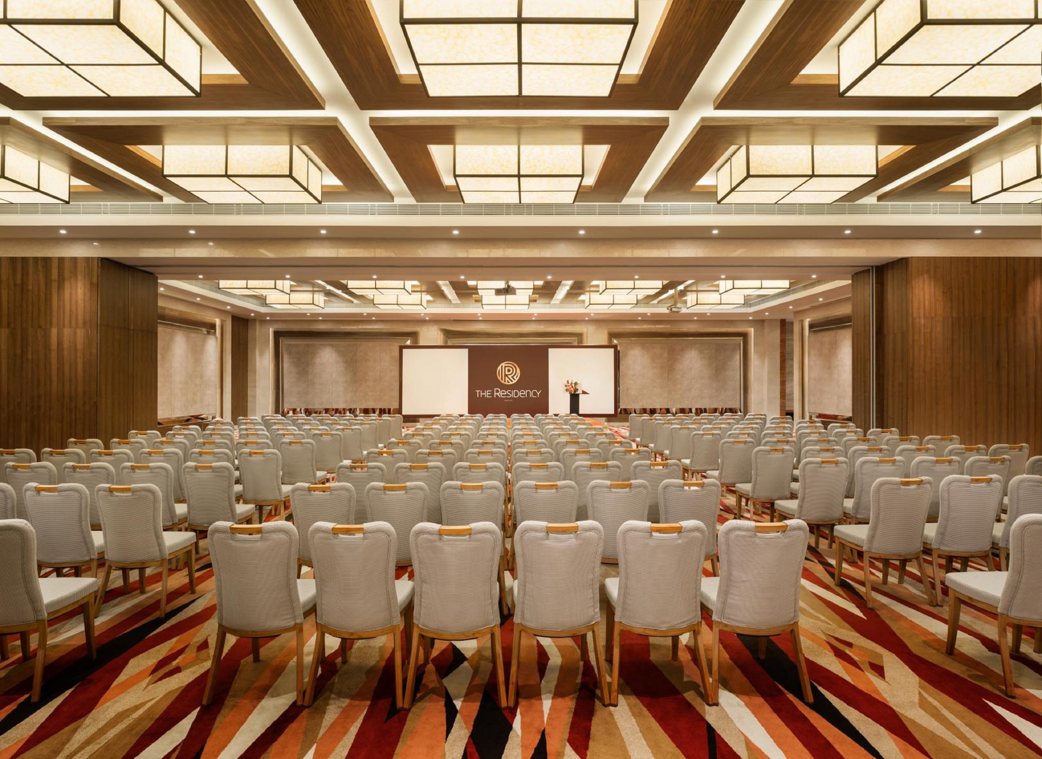 A conference room with rows of chairs facing a stage with a presentation screen and a podium.