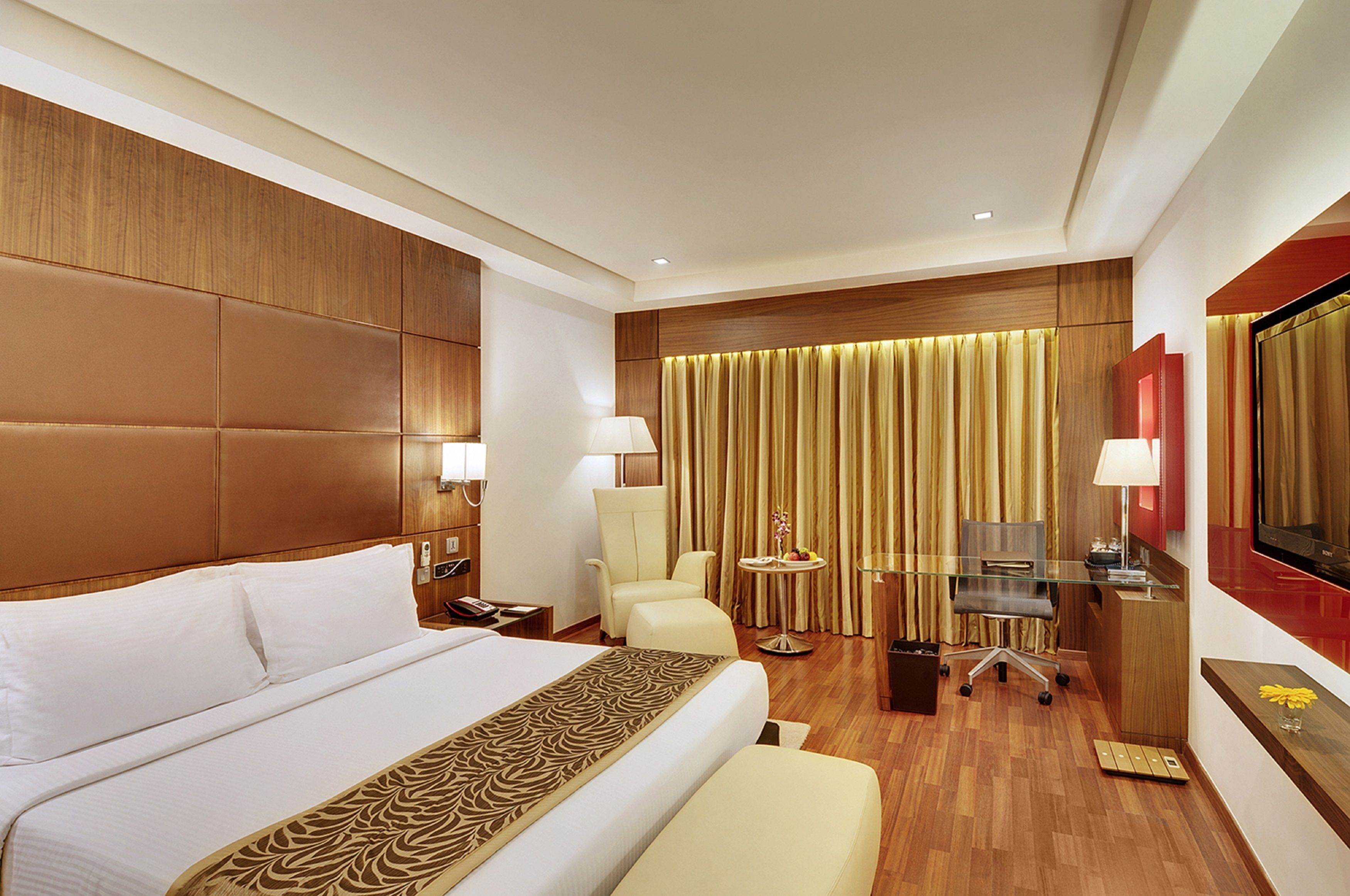 A hotel room with a large bed, a desk, a chair, a TV, and a curtain backdrop.