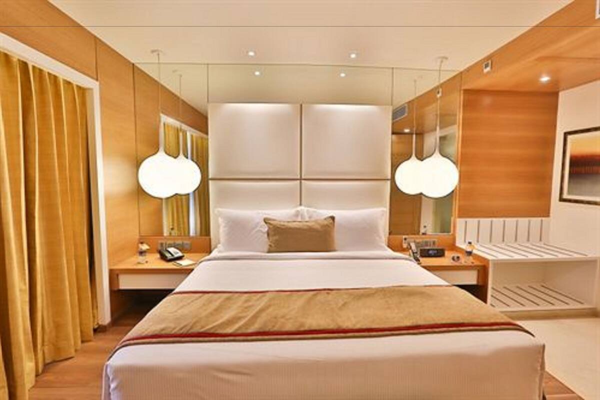 A modern hotel room with a large bed, bedside tables, a desk, and a mirror.