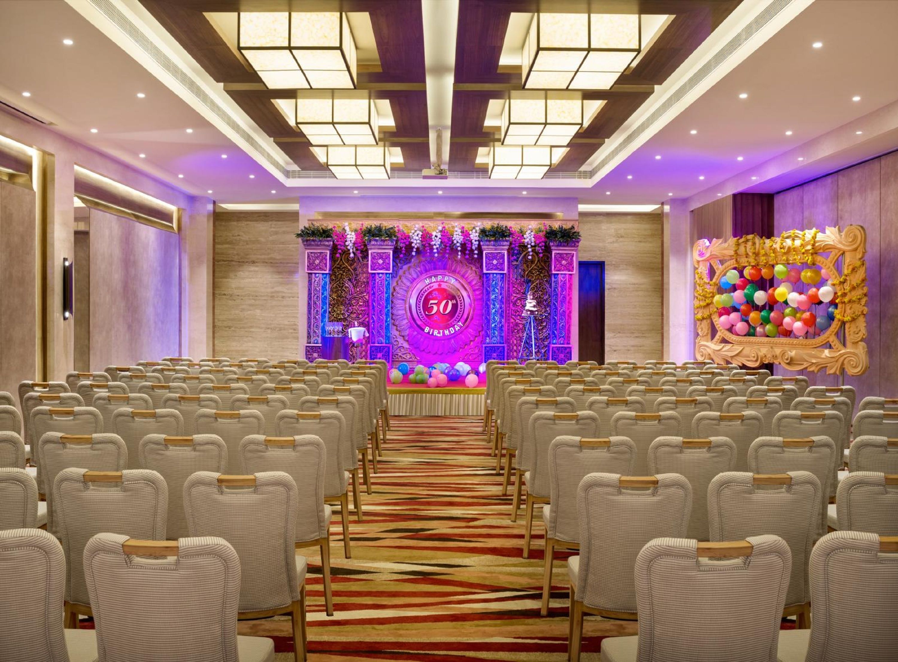 A conference room with rows of chairs facing a stage with a '50th Birthday' backdrop.