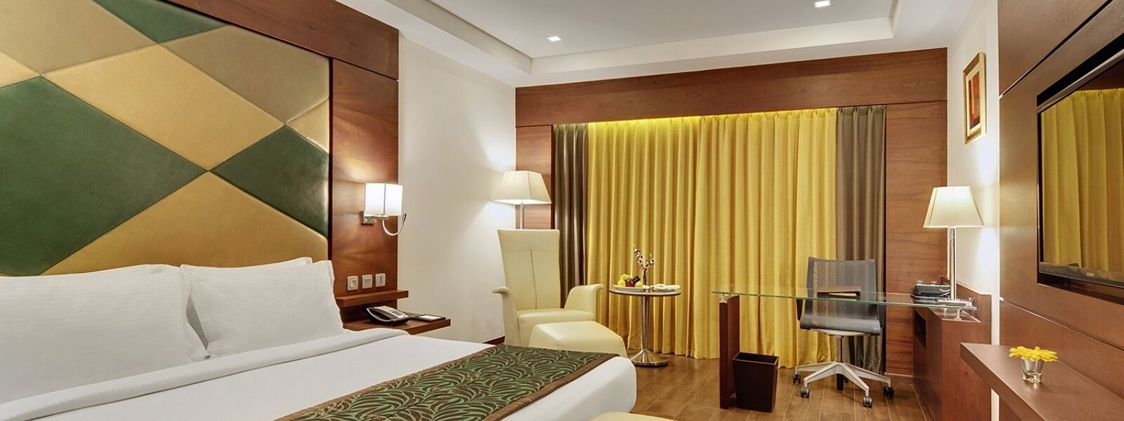 A hotel room with a bed, a desk, a chair, a TV, and a curtain.