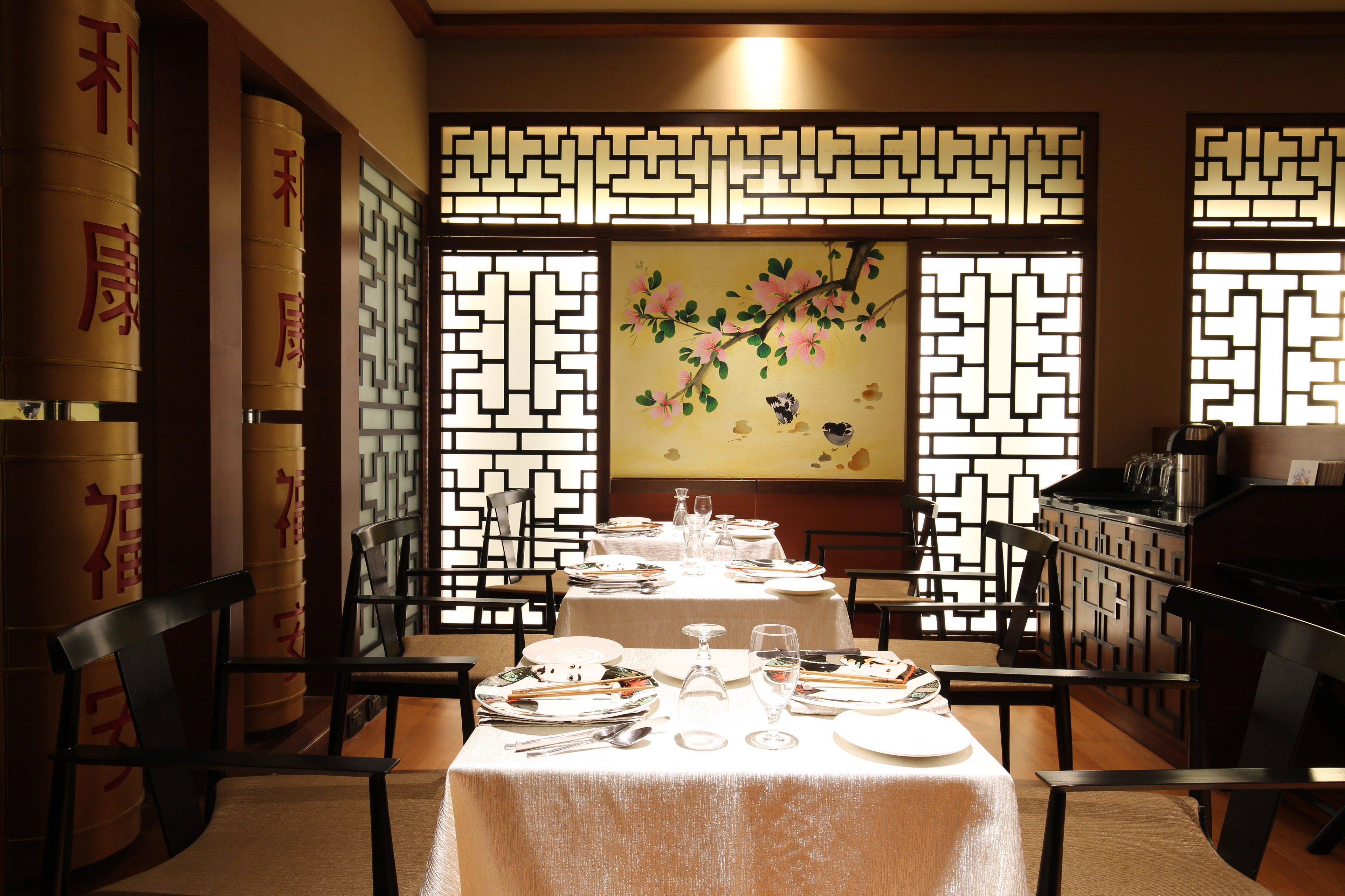 A traditional Chinese dining room with tables set for a meal, decorative screens, and calligraphy on the walls.