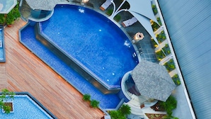 Una piscina en la azotea con terraza de madera, sillas de descanso y sombrillas.