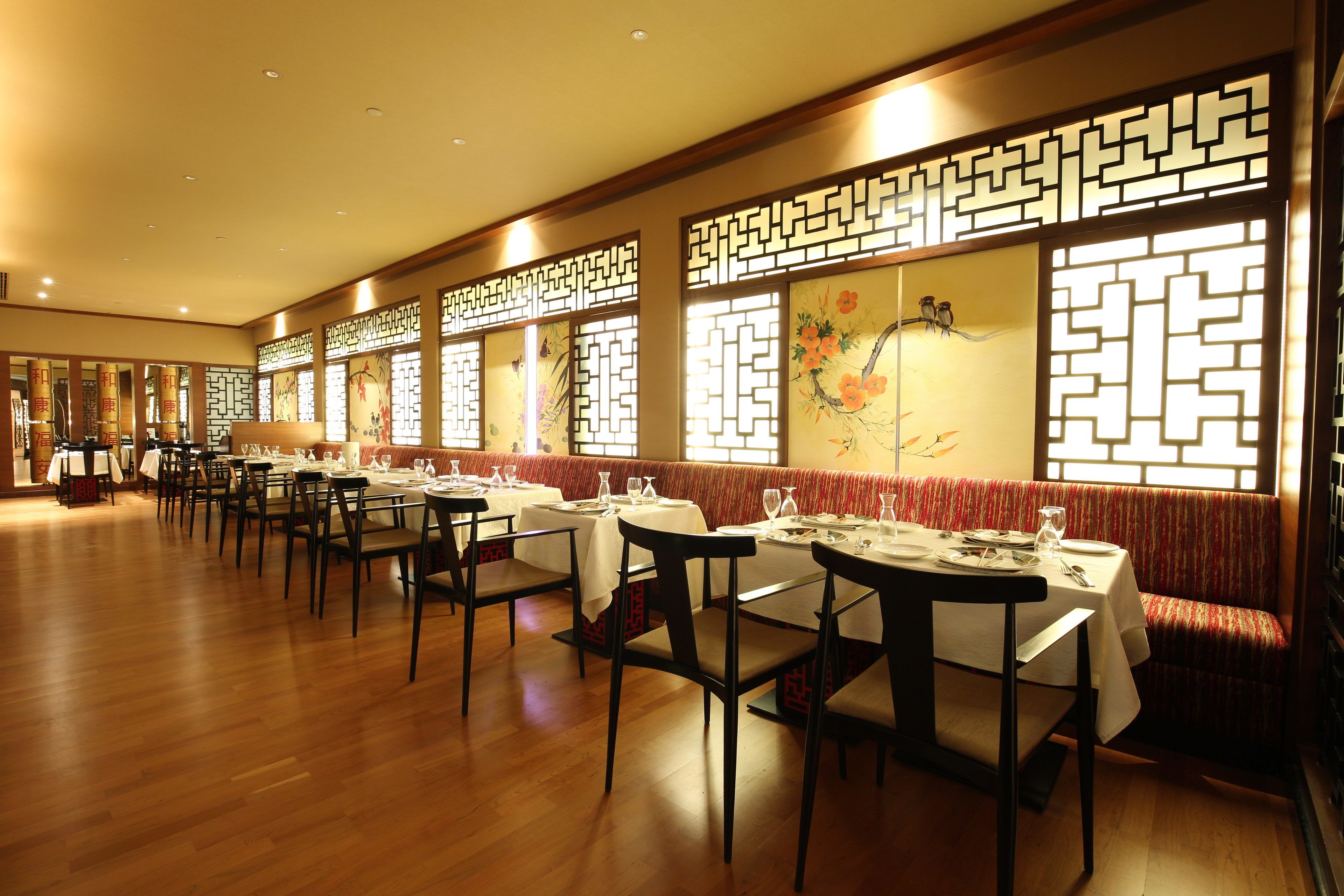 A restaurant with wooden flooring, tables set with white tablecloths, and traditional Chinese decorative screens.