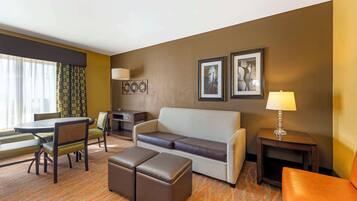 Habitación de hotel con sofá, reposapiés, mesa de comedor, sillas, una lámpara y cuadros en la pared.