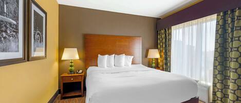 A hotel room with a large bed, two bedside tables with lamps, a headboard, and a window with curtains.