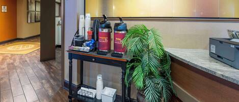 Een receptiezone met een koffiehoek, een plant en een bord voor 'SUNDAY SHOP'.