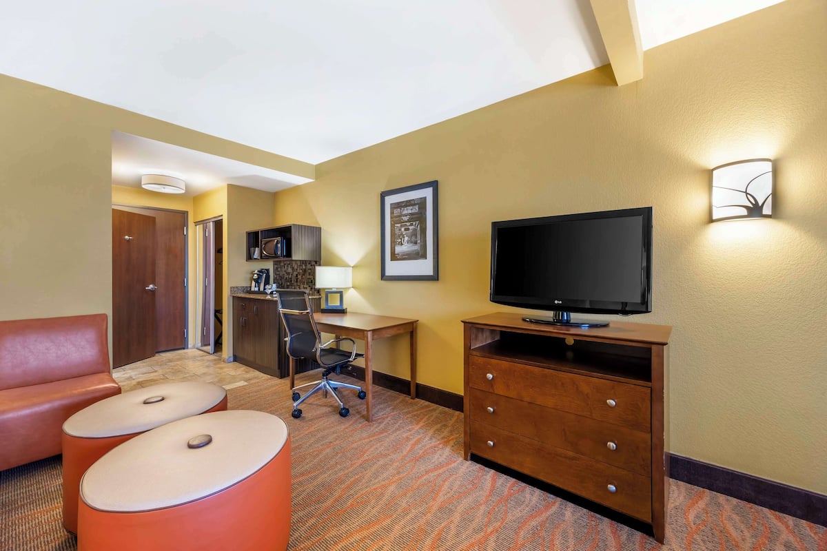 A hotel room with a sofa, a desk with a computer, a television, and a cabinet.