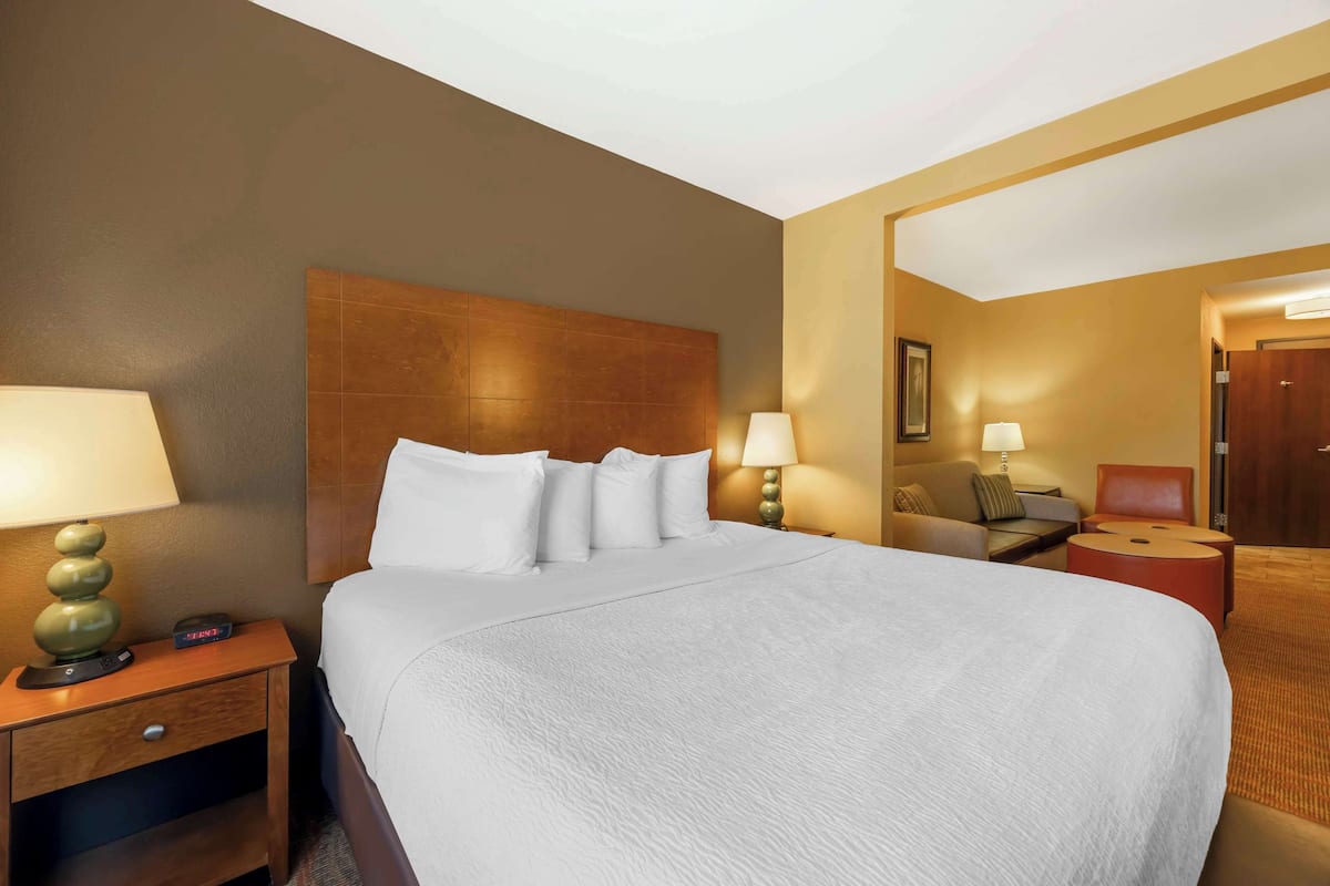 A hotel room with a large bed, a nightstand with a lamp, a small table with a lamp, and a mirror on the wall.