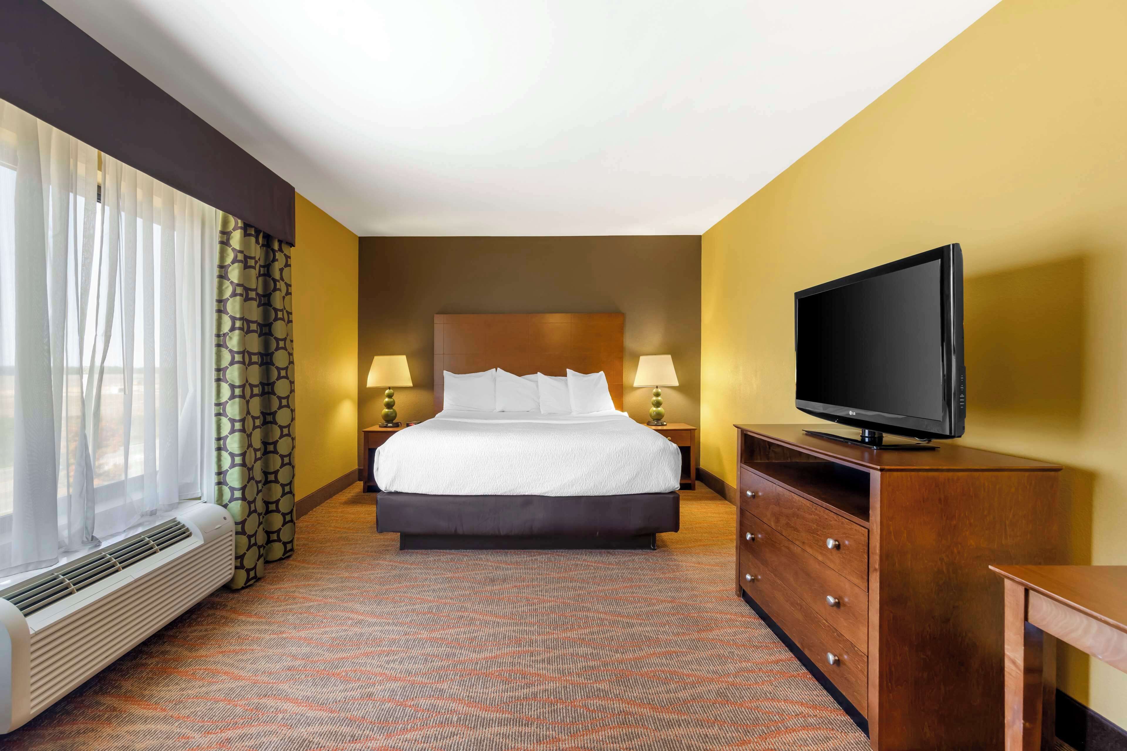 Habitación de hotel con cama, televisor sobre una cómoda de madera, calefacción y una ventana con cortinas.