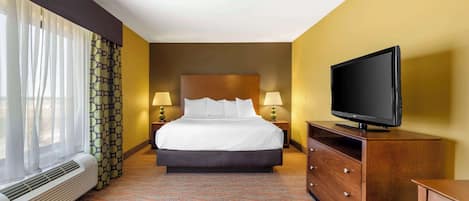 A hotel room with a bed, a television on a wooden dresser, a heater, and a window with curtains.