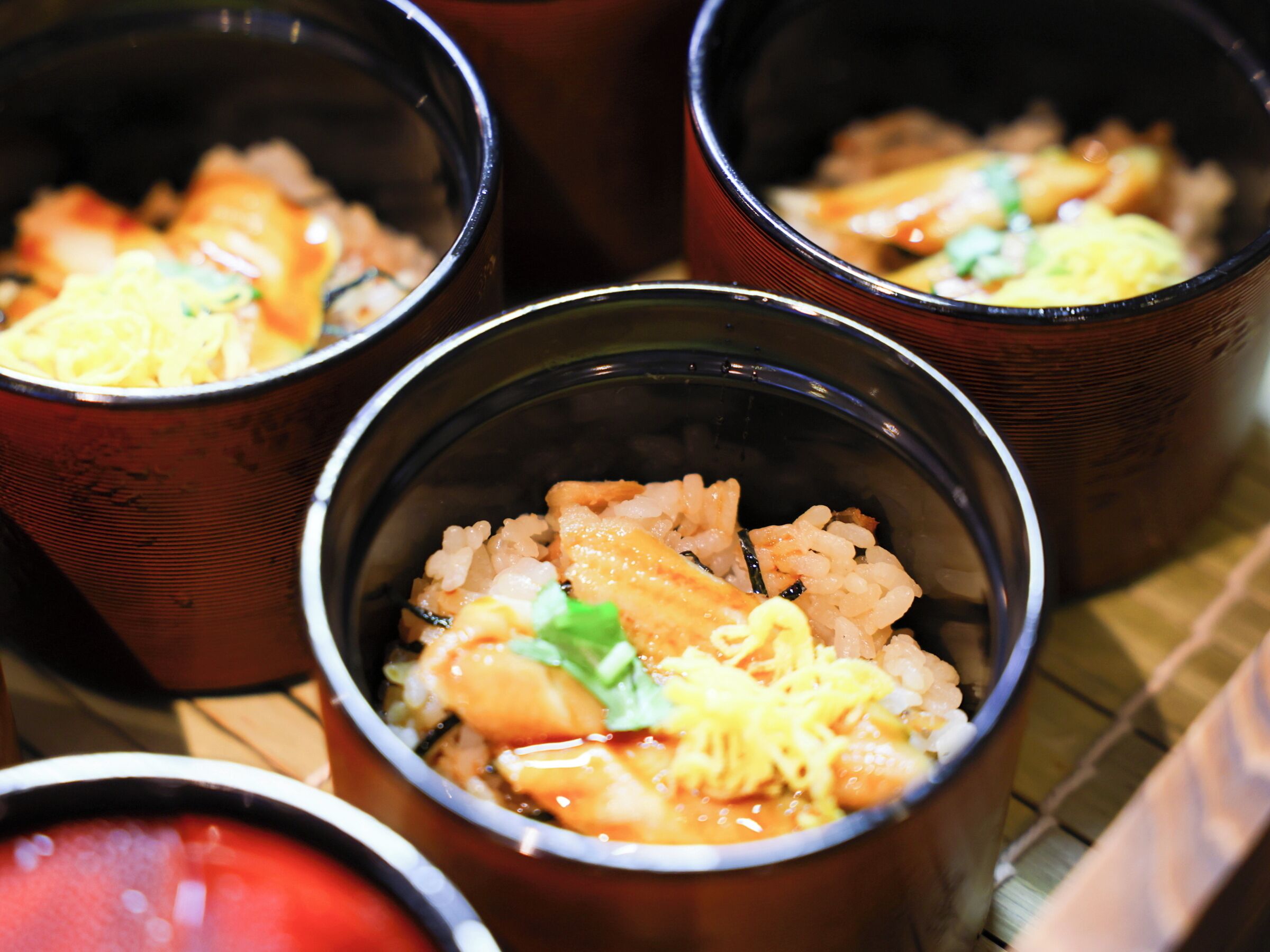 Three bowls of food with rice, vegetables, and fish.