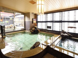Un tradizionale onsen giapponese con interni in legno, una sorgente termale in pietra e vista sul giardino esterno.